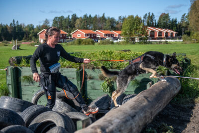 Vrouw met haar hond tijdens een obstakelrace, de hond is uitgerust met materiaal van Non-stop dogwear.