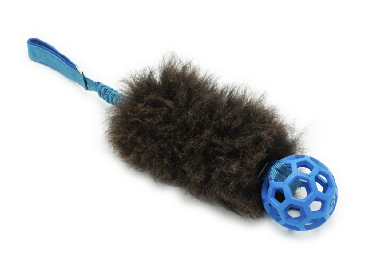 Productafbeelding van het Wooly trekspeeltje van Zayma Craft, met een blauwe hol-ee roller bal, bruine schapenvacht en een elastisch bungee handvat