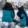 Vrouw met hond in de sneeuw in de bergen, elk met een blauwe winterjas, ze geven een kusje aan elkaar.