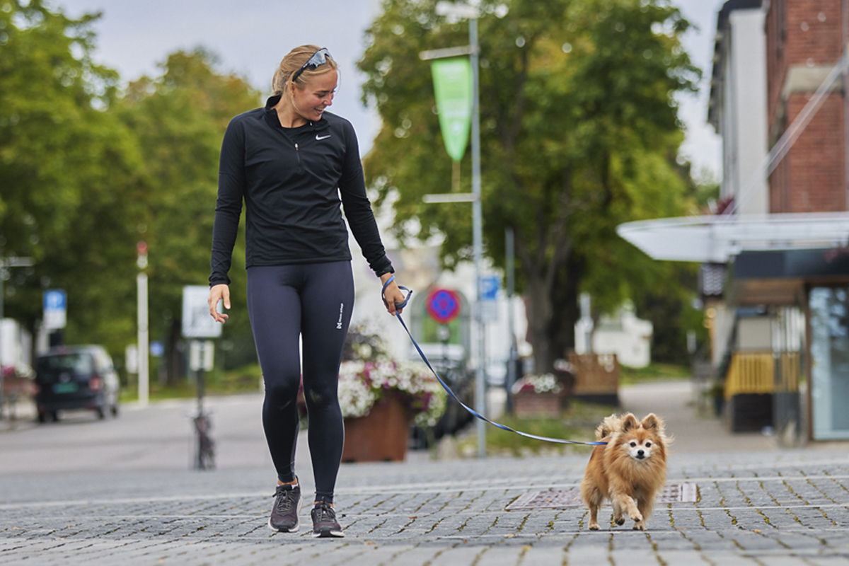 Vrouw wandelt met bruin keeshondje aan de leiband in de stad